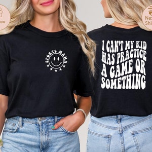 May include: Black t-shirt with white text that reads "I can't my kid has practice a game or something" on the back and a white smiley face with the text "Sports Mama" on the front.