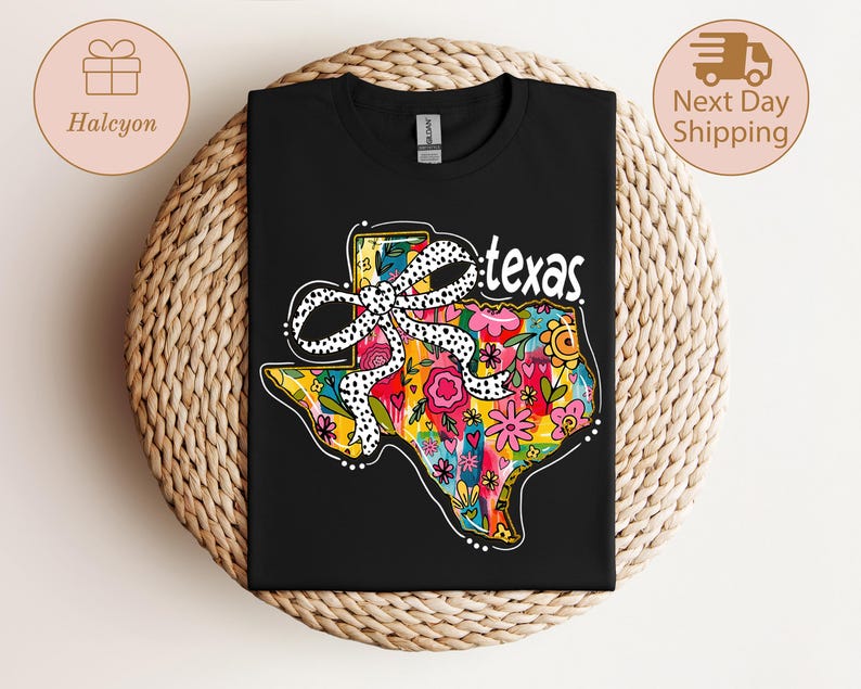 以下が含まれることがあります： カラフルなテキサス州のアウトラインが特徴の黒いTシャツ。花柄と水玉模様のリボンが描かれています。「texas」の文字が白で書かれています。Tシャツは織り込まれた表面に表示されています。