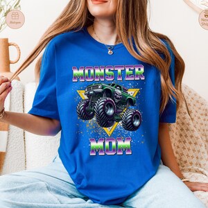 May include: Royal blue t-shirt featuring a graphic of a green monster truck with a skull design, set against a yellow triangle. The text "MONSTER MOM" is displayed in a vibrant, multi-colored font.