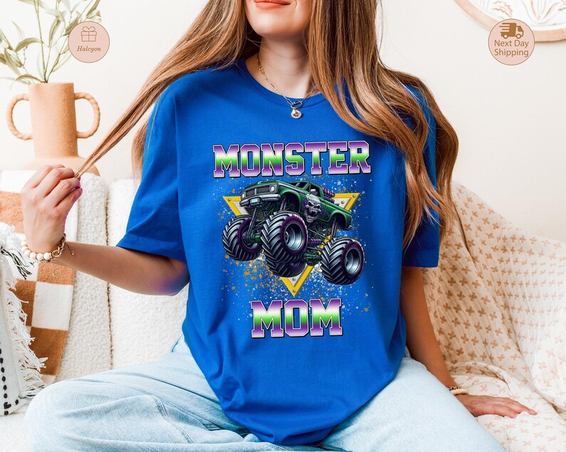 May include: Royal blue t-shirt featuring a graphic of a green monster truck with a skull design, set against a yellow triangle. The text "MONSTER MOM" is displayed in a vibrant, multi-colored font.