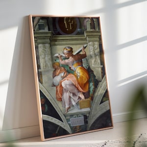 May include: Framed print of a Renaissance-style artwork. The image features figures in flowing robes, with a color palette of oranges, pinks, and blues. The artwork is set within an ornate architectural background, and the frame is a light brown color.