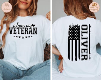 May include: White t-shirt with the text "i love my VETERAN" in black, with a heart and stars. The back of the shirt features a distressed American flag design with the name "OLIVER" in white.