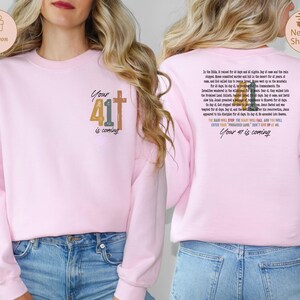 May include: Pink sweatshirt with the text "Your 41 is coming" and a cross on the front. The back of the sweatshirt has a bible verse with the text "Your 41 is coming" at the bottom.