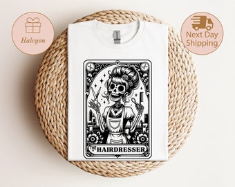 May include: A black and white illustration of a skeleton dressed as a hairdresser. The skeleton is holding scissors and a comb. The illustration is framed in a decorative border and the text "The Hairdresser" is below the image.
