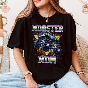 May include: Black t-shirt with a graphic of a green monster truck and the words "MONSTER MOM" in purple and green. The design includes a yellow triangle and a splatter effect.