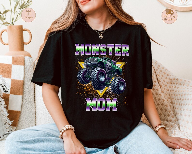 May include: Black t-shirt with a graphic of a green monster truck and the words "MONSTER MOM" in purple and green. The design includes a yellow triangle and a splatter effect.