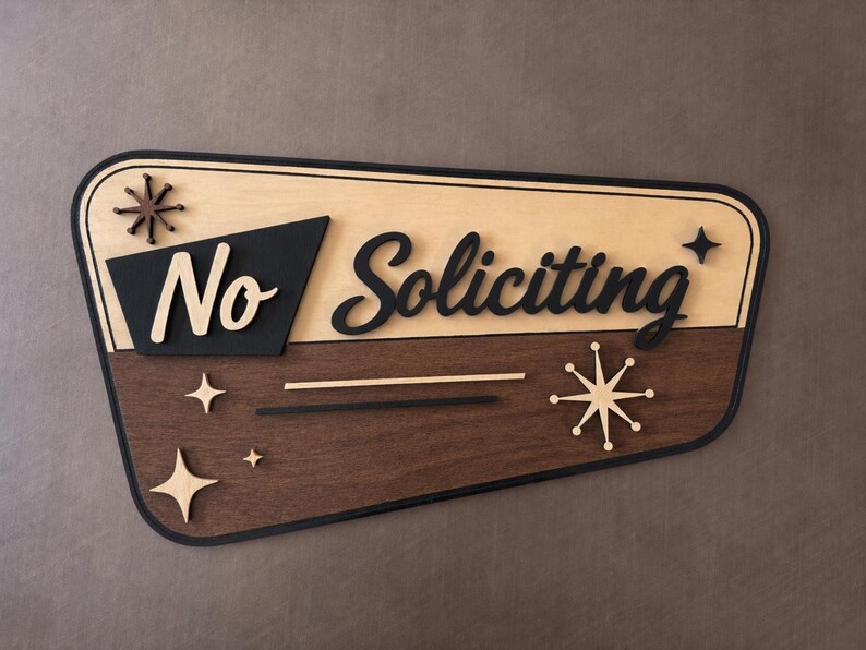May include: A trapezoidal wooden sign with a black border, featuring the text "No Soliciting" in a layered design. The top section is light wood, the bottom is dark wood, and the sign is decorated with starburst shapes in black and light wood.