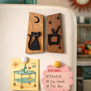 May include: Wooden refrigerator magnets with a mid-century modern theme. Includes a black cat, a television, a bar cart, and a pink flower-shaped to-do list. The to-do list includes "Dentist", "Car Wash", and "Tiki Bar".