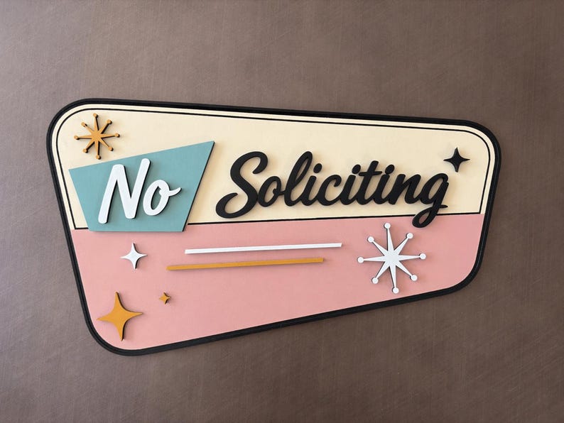 May include: A trapezoidal wall sign with a cream and pink background featuring the text No Soliciting in black and white script. The design includes a teal accent shape, gold and white starburst icons, and two horizontal lines in white and gold.
