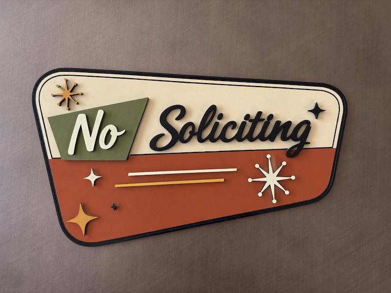 May include: A trapezoidal wall sign with a cream top and terracotta bottom section. It features the text "No Soliciting" in black and white script, accented by olive green geometric shapes and several gold and white starburst icons.
