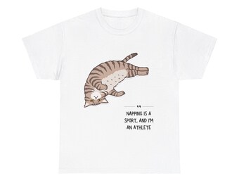 May include: White t-shirt featuring a cartoon cat in a playful pose. The cat has brown and tan stripes. Text below the cat reads, "Napping is a sport, and I'm an athlete."