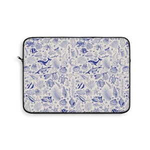 May include: A laptop sleeve featuring a repeating pattern of marine life in shades of blue and white. The design includes whales, fish, jellyfish, shells, and coral, creating an underwater theme. The sleeve has a black zipper and trim.