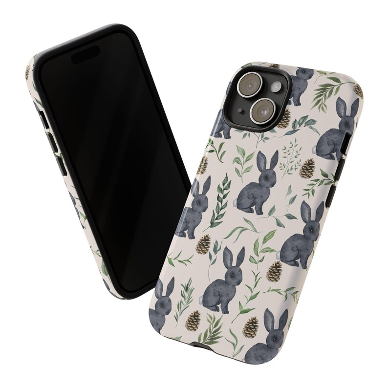 May include: A white phone case with a black border and a pattern of watercolor bunnies, leaves, and pine cones. The case has a cutout for the camera lens.