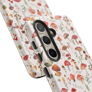 May include: A white phone case with a colorful mushroom and floral pattern. The case has a black camera cutout and a raised lip around the edges.