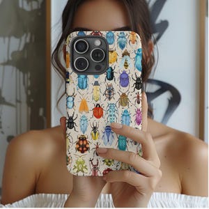 Pode incluir: Capa de telemóvel com fundo creme, decorada com um padrão de escaravelhos coloridos. Os escaravelhos são de várias cores, incluindo azul, amarelo, vermelho e preto. A capa tem um recorte para a câmara e um design elegante.