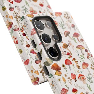 May include: A white phone case with a pattern of red and brown mushrooms and green leaves. The case has a cutout for the camera lens.