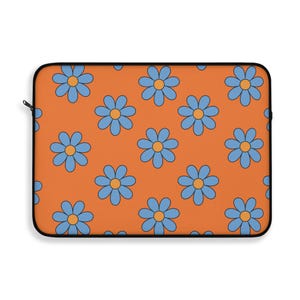 May include: An orange laptop sleeve with a black zipper and trim. The sleeve is covered in a repeating pattern of blue flowers with orange centers. The design is reminiscent of the 1970s.