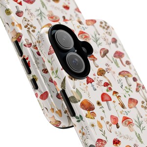 May include: A white phone case with a pattern of red and brown mushrooms, green leaves, and yellow flowers. The case has a black camera lens cutout.