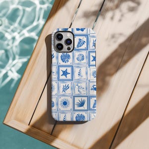 Może przedstawiać: Białe etui na telefon z niebiesko-białym wzorem płytek z motywami morskimi i tropikalnymi. Etui ma wycięcie na aparat telefonu.