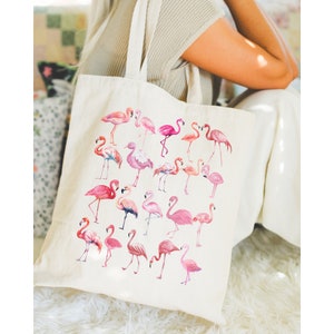 May include: A cream-coloured tote bag with a watercolour design of pink flamingos. The flamingos are in various poses and shades of pink, creating a lively pattern. The bag has two handles for carrying, ideal for shopping or everyday use.