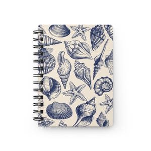 May include: A spiral bound notebook with a cream-colored cover featuring a repeating pattern of blue seashells and starfish.