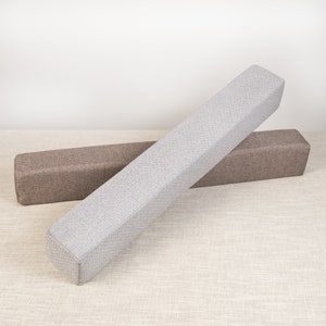 May include: Two rectangular cushions, one gray and one brown, are lying on a light beige surface. The cushions are made of a textured fabric and are both about 18 inches long.