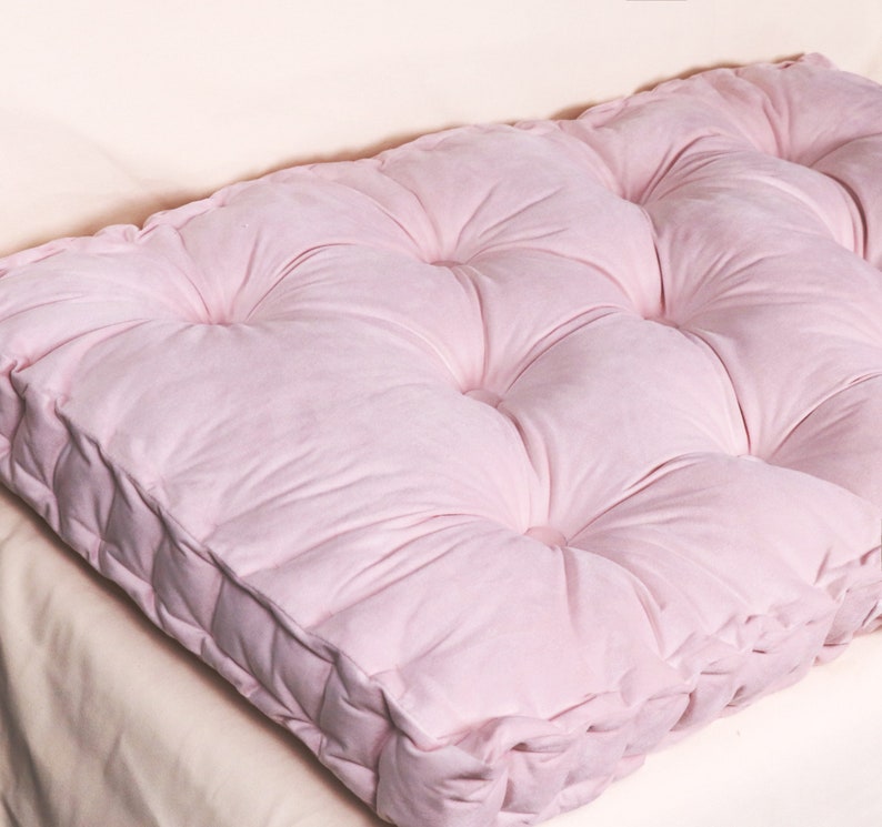 Puede incluir: Un coj&iacute;n de suelo rosa capiton&eacute; con forma cuadrada y textura suave y mullida.
