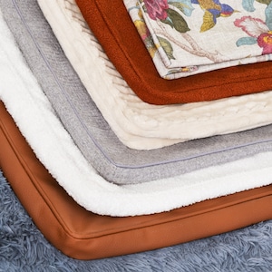 May include: A stack of six different fabric swatches in various colors and textures, including a floral patterned fabric, a brown fabric, a white fabric, a gray fabric, a white fabric, and a brown fabric.