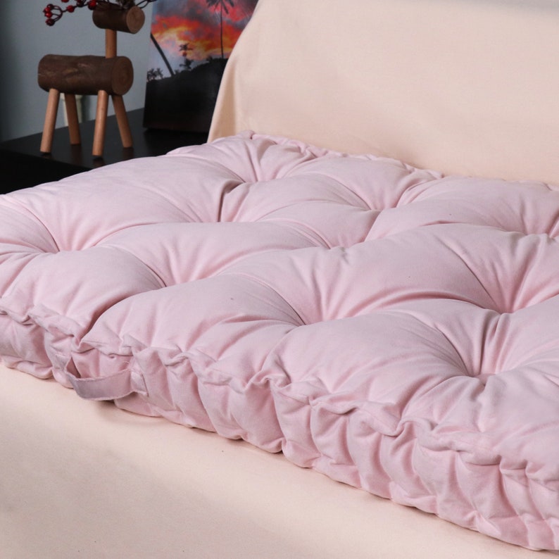 Puede incluir: Un coj&iacute;n de suelo rosa capiton&eacute; con un dise&ntilde;o de botones. El coj&iacute;n est&aacute; hecho de una tela suave y mullida y tiene un aspecto simple y elegante.