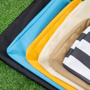 May include: A collection of folded fabric in various colors, including black, light blue, yellow, cream, tan, and a black and white striped pattern. The fabrics are arranged diagonally, showcasing their different hues and textures against a green background.