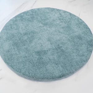 May include: A round, teal blue cushion with a textured fabric surface.
