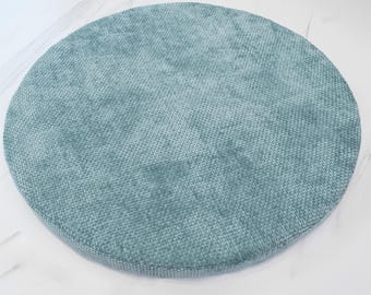 May include: A round, teal blue cushion with a textured fabric surface.