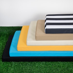 May include: Four different sized rectangular cushions stacked on top of each other. The top cushion is black and white striped, the next is beige, the next is yellow, and the bottom cushion is blue.