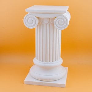 May include: White ceramic pedestal with a square base and a fluted column topped with a square platform. The pedestal is a decorative element for displaying objects.