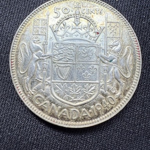 May include: A silver Canadian 50-cent coin with the year 1940 and the text "50 CENTS CANADA 1940" around the edge. The coin features a coat of arms with a lion and a unicorn on either side.