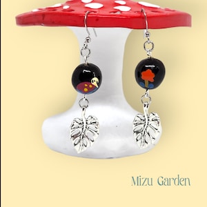 May include: A pair of silver earrings with black beads and silver leaf charms. The beads are hand-painted with a ladybug and a small tree.