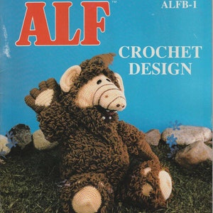 Puede incluir: Patrón de crochet para hacer un muñeco ALF. El patrón es de Millcraft, Inc. y presenta un muñeco ALF de crochet marrón y beige sentado en hierba verde.