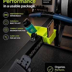 Op de afbeelding: Een zwarte roeimachine met een neon groene organizer met een turquoise waterfles en een houten telefoonhoesje. De machine heeft een zwarte voetsteun en een blauwe handgreep. Tekst op de machine zegt "Concept". De afbeelding bevat ook de tekst "Style and Performance".