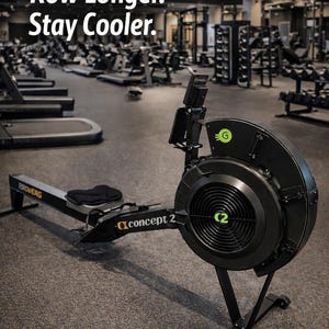 May include: A black Concept2 rowing machine with a fan and digital display is positioned in a gym. The text "Row Longer. Stay Cooler." is displayed in white. Other exercise equipment is visible in the background.