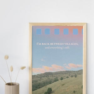 Peut inclure: Une impression encadrée avec une citation qui dit "Je suis de retour entre les villages, et tout est toujours." L'impression présente une photographie d'une colline verdoyante avec un ciel bleu et des nuages blancs.