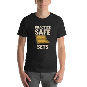 Könnte beinhalten: Ein dunkelgraues T-Shirt mit dem Text "PRACTICE SAFE SETS" in Weiß und einer Grafik einer Holzkiste mit einem gebrochenen Scharnier.