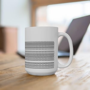 May include: White ceramic mug with a black geometric pattern of lines and shapes. The mug has a handle on the right side.