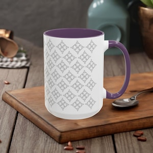 Puede incluir: Taza de cerámica blanca con interior y asa morados. La taza presenta un patrón repetido de gestos de manos estilizados en negro. La taza está sobre una tabla de cortar de madera.