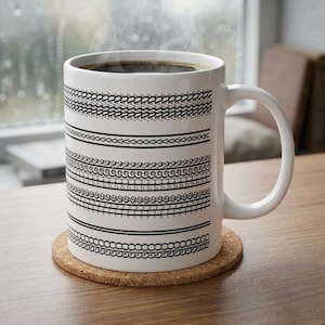 May include: A white ceramic coffee mug filled with dark coffee, resting on a cork coaster. The mug features a series of black tire tread patterns around its exterior. Steam rises from the coffee, suggesting it is hot.
