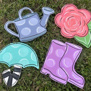 May include: A set of four decorative wooden cutouts featuring a light blue polka dot watering can, a pink flower with green leaves, a teal polka dot umbrella with a black and white striped handle, and a pair of purple polka dot rain boots.
