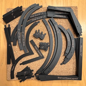Puede incluir: Una colección de piezas de vidrio tintado negro, que incluyen círculos, óvalos, hexágonos, cuadrados y corazones. Las piezas están etiquetadas con su forma y tamaño en pulgadas. El texto "StainedGlassLayout" es visible en la esquina inferior derecha.