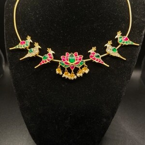 May include: A gold choker necklace with a lotus flower design in the center and five birds on either side. The birds are decorated with green and pink enamel and have clear stones for eyes.