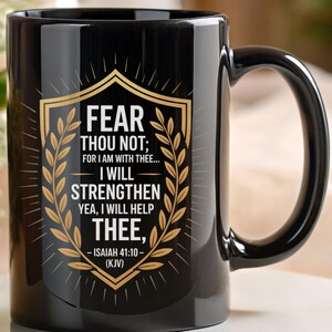 Może przedstawiać: Czarny ceramiczny kubek ze złotym wzorem tarczy i napisem "FEAR THOU NOT; FOR I AM WITH THEE... I WILL STRENGTHEN YEA, I WILL HELP THEE, -ISAIAH 41:10- (KJV)". Kubek ma czarny uchwyt i stoi na białej powierzchni.