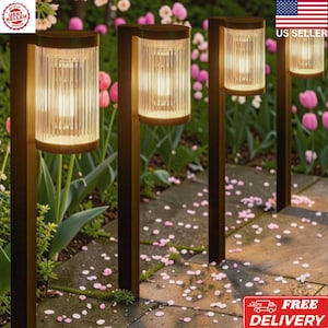 May include: A set of four outdoor path lights featuring dark brown metal posts and cylindrical, vertically ribbed glass shades. Each fixture emits a warm, glowing light from an internal bulb, illuminating the surrounding garden area.