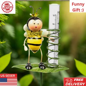 May include: A whimsical bee-shaped rain gauge with a yellow and black striped body, holding a clear tube with inch measurements. The gauge is mounted on a green leaf and has the text "Funny Gift :)".